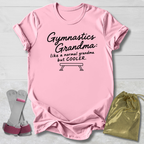A pink short-sleeve graphic T-shirt laid flat on a light wood background, with black text reading 'Gymnastics Grandma: like a normal grandma but COOLER.' and a bench outline.