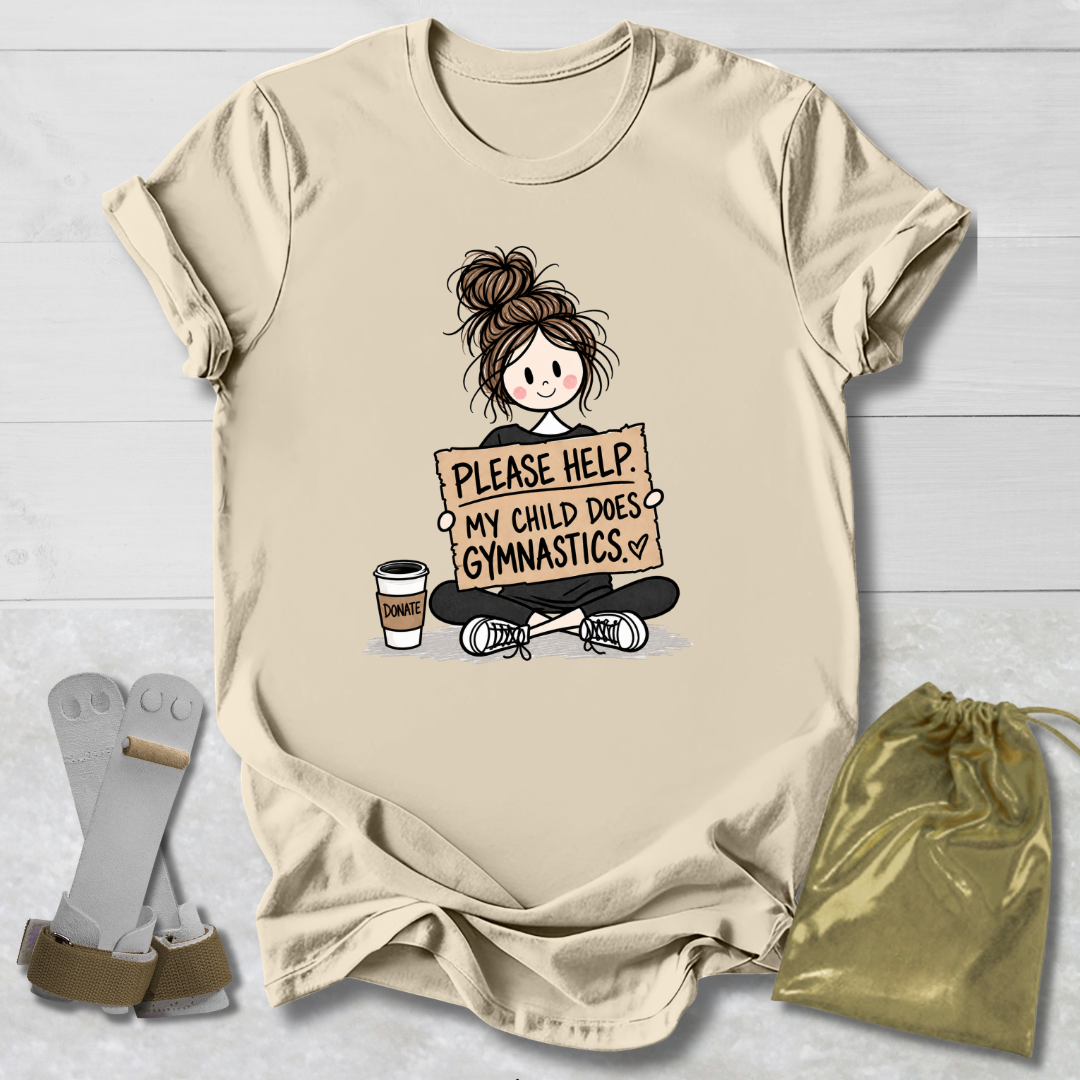 A beige graphic t-shirt laid flat on a white wood background, featuring a cartoon illustration of a gymnast holding a sign that reads 'PLEASE HELP MY CHILD DOES GYMNASTICS' with a coffee cup next to her. A pair of gray and tan athletic socks and a gold drawstring bag are placed beside the shirt.