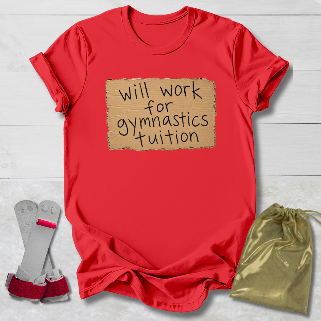 A red short-sleeve t-shirt with a cardboard-texture graphic that reads 'will work for gymnastics tuition' in black handwritten-style text. The shirt is laid flat on a white wood-plank background, styled with a pair of gymnastics bars on the left and a shiny gold drawstring bag on the right.