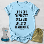 A light blue graphic T-shirt laid flat on a white wood background, with bold black text reading “LET’S GET TO PRACTICE EARLY AND DO EXTRA CONDITIONING” and a small “-Psychopaths” signature below. A gray and blue pair of stretching straps and a gold drawstring pouch are placed beside the shirt as styling props.