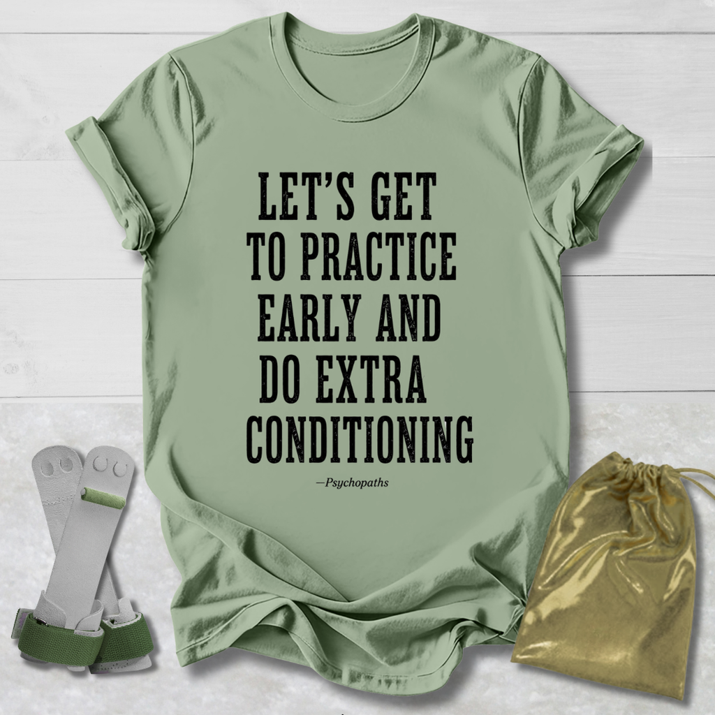A sage green graphic t-shirt with black text reading 'LET'S GET TO PRACTICE EARLY AND DO EXTRA CONDITIONING - Psychopaths' is displayed on a white wood background, styled with a pair of white and green athletic support sleeves on the left and a gold drawstring pouch on the right.