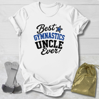 A white short-sleeve T-shirt laid flat on a light wood background, printed with the phrase 'Best Gymnastics Uncle Ever!' in black and blue lettering with a blue star. A gray strap and a gold drawstring pouch are placed beside the shirt as props.