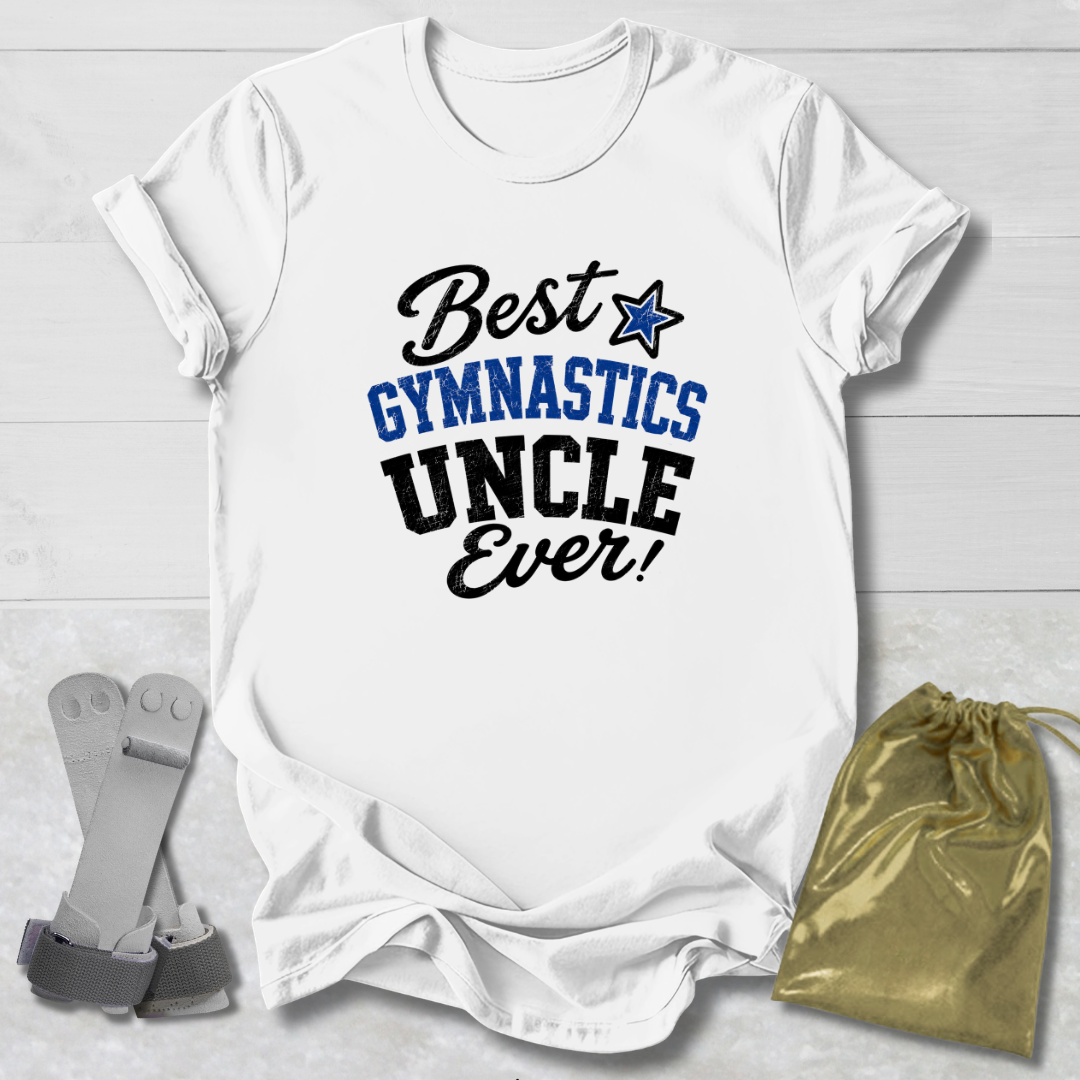 A white short-sleeve T-shirt laid flat on a light wood background, printed with the phrase 'Best Gymnastics Uncle Ever!' in black and blue lettering with a blue star. A gray strap and a gold drawstring pouch are placed beside the shirt as props.
