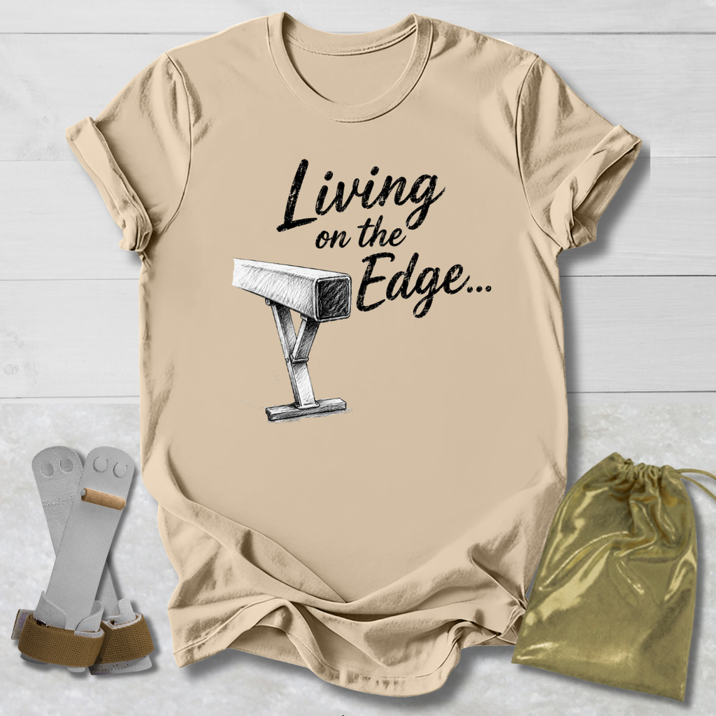 Beige balance beam graphic T-shirt laid flat on a white wood background, printed with the words 'Living on the Edge.