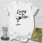 white graphic T-shirt laid flat on a white wood background, printed with the words 'Living on the Edge.