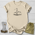 Natural t-shirt with a black line art graphic of a frog doing a handstand, displayed on a white wood background alongside a gold drawstring bag and a pair of white and green wristbands.