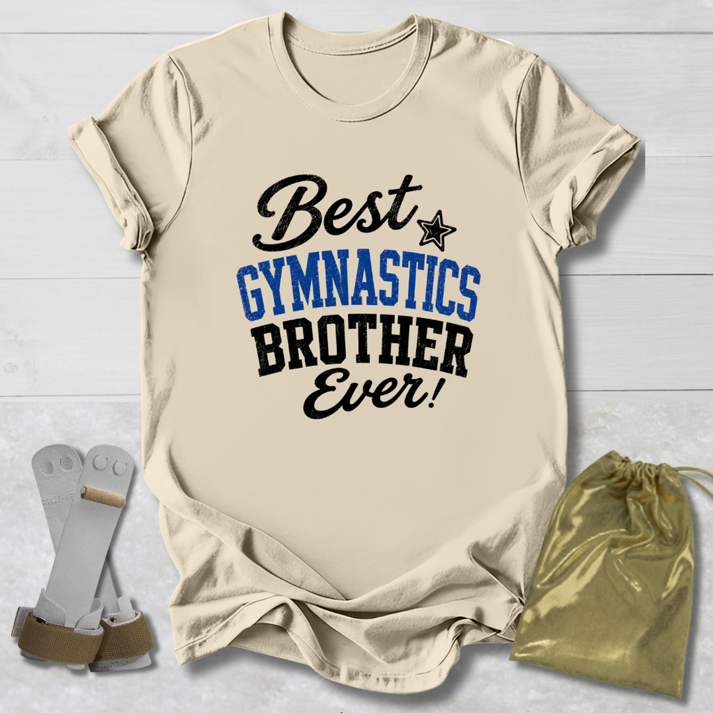 Beige short-sleeve T-shirt laid flat on a light wood background, printed with the phrase 'Best GYMNASTICS BROTHER Ever!' in black and blue lettering. A small black star appears between 'Best' and 'GYMNASTICS.