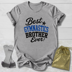 Gray short-sleeve T-shirt laid flat on a light wood background, printed with the phrase 'Best GYMNASTICS BROTHER Ever!' in black and blue lettering. A small black star appears between 'Best' and 'GYMNASTICS.