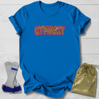 A bright blue short-sleeve t-shirt laid flat on a white wood background, featuring the word 'GYMNIST' across the chest in leopard-print letters outlined in pink. A gold drawstring pouch and a pair of blue-and-white wrist wraps are placed beside the shirt as styling props.