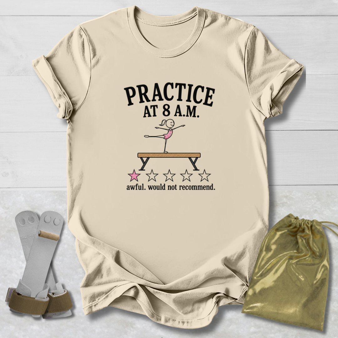 A beige graphic t-shirt laid flat on a white wood background, featuring a gymnastics-themed print that reads 'PRACTICE AT 8 A.M.