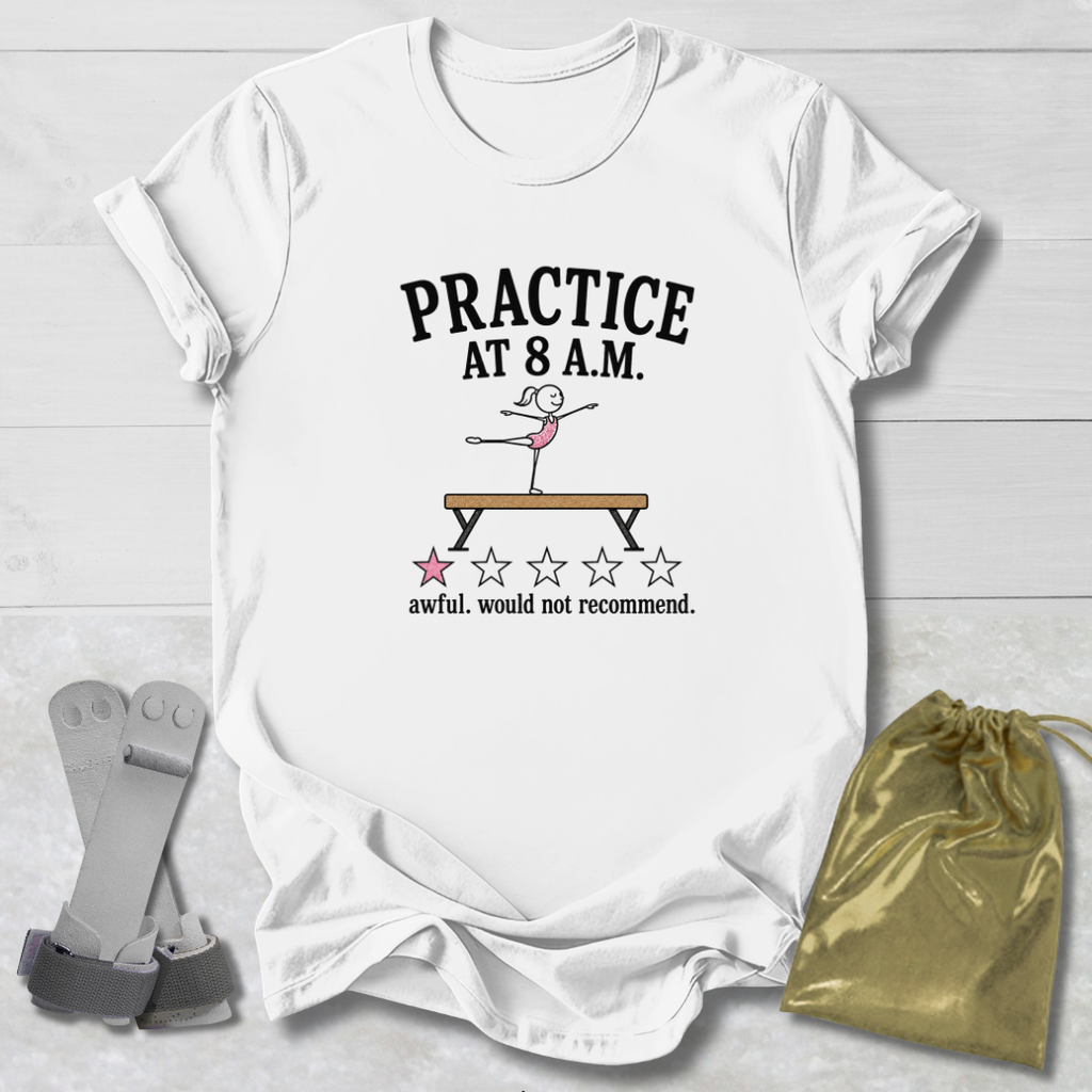 A white graphic t-shirt laid flat on a light wood background, featuring the text 'PRACTICE AT 8 A.M.