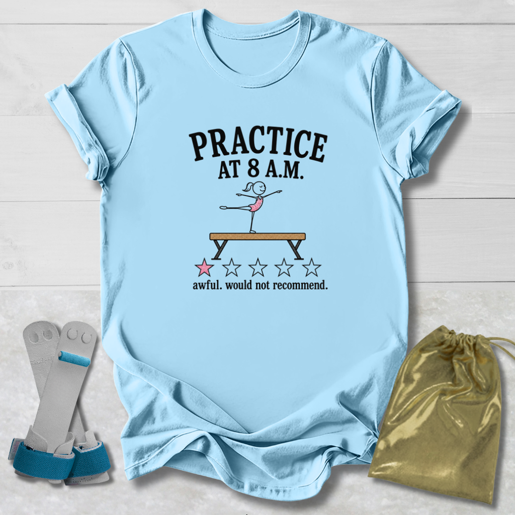 A light blue graphic t-shirt laid flat on a white wood background, featuring a gymnastics-themed print that reads 'PRACTICE AT 8 A.M.
