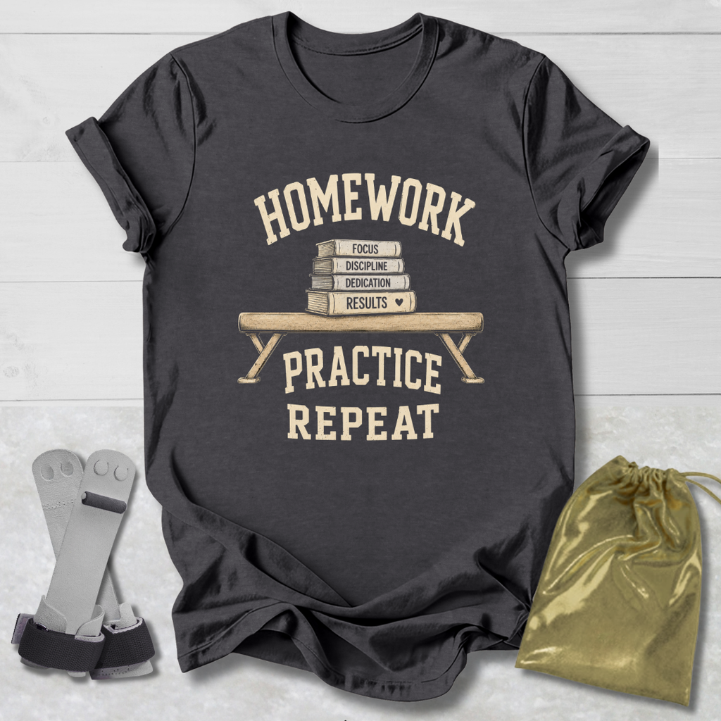 A dark charcoal gray graphic t-shirt laid flat on a white wood background, featuring a cream-colored print that reads 'HOMEWORK PRACTICE REPEAT' around an illustration of stacked books on a bench. A gold drawstring pouch and a pair of gray and black athletic shoes are placed beside the shirt as props.