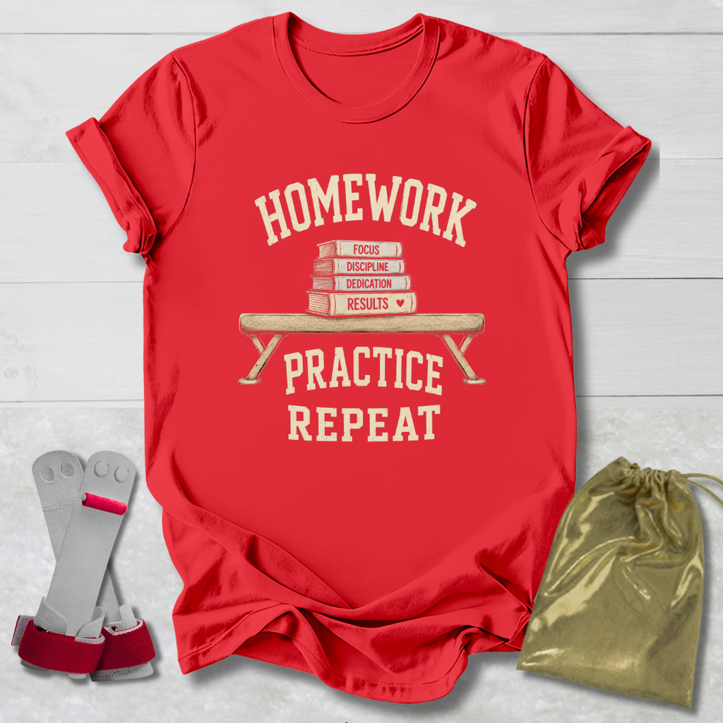 A red short-sleeve graphic T-shirt laid flat on a light wood background, with a cream-colored school-themed print reading 'HOMEWORK PRACTICE REPEAT' around an illustration of stacked books on a bench. A gray and pink shoe accessory and a gold drawstring pouch are placed beside the shirt as styling props.