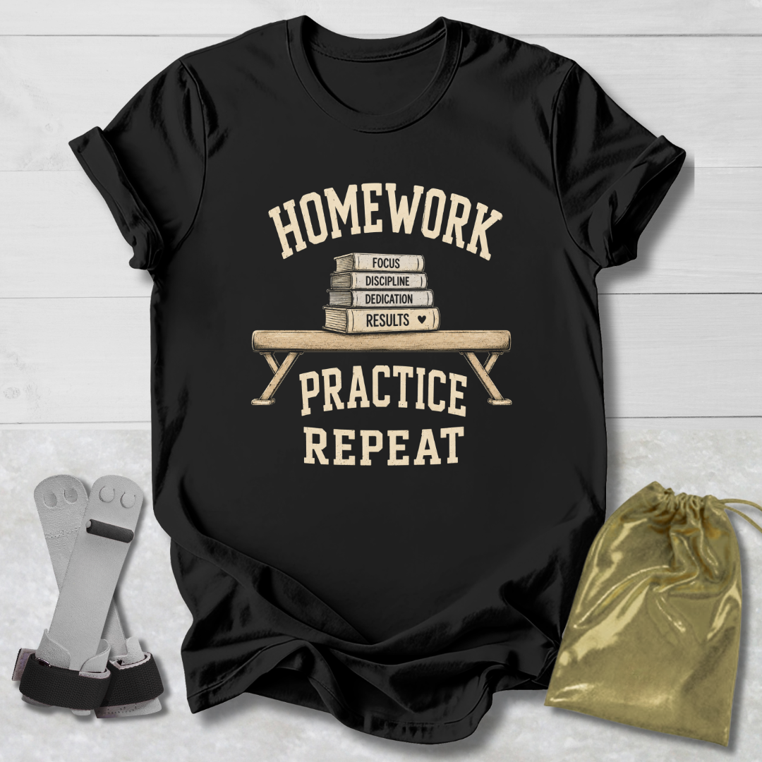 A black graphic t-shirt laid flat on a light wood background, featuring a cream-colored print that reads 'HOMEWORK PRACTICE REPEAT' with a stack of books and a pencil. A gray resistance band is placed to the left, and a shiny gold drawstring pouch is on the right.
