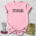A light pink short-sleeve t-shirt with the black text 'Will trade brother for a new leopard' printed on the chest, displayed on a light gray wood background alongside a pair of gray and pink boxing gloves and a gold drawstring bag.
