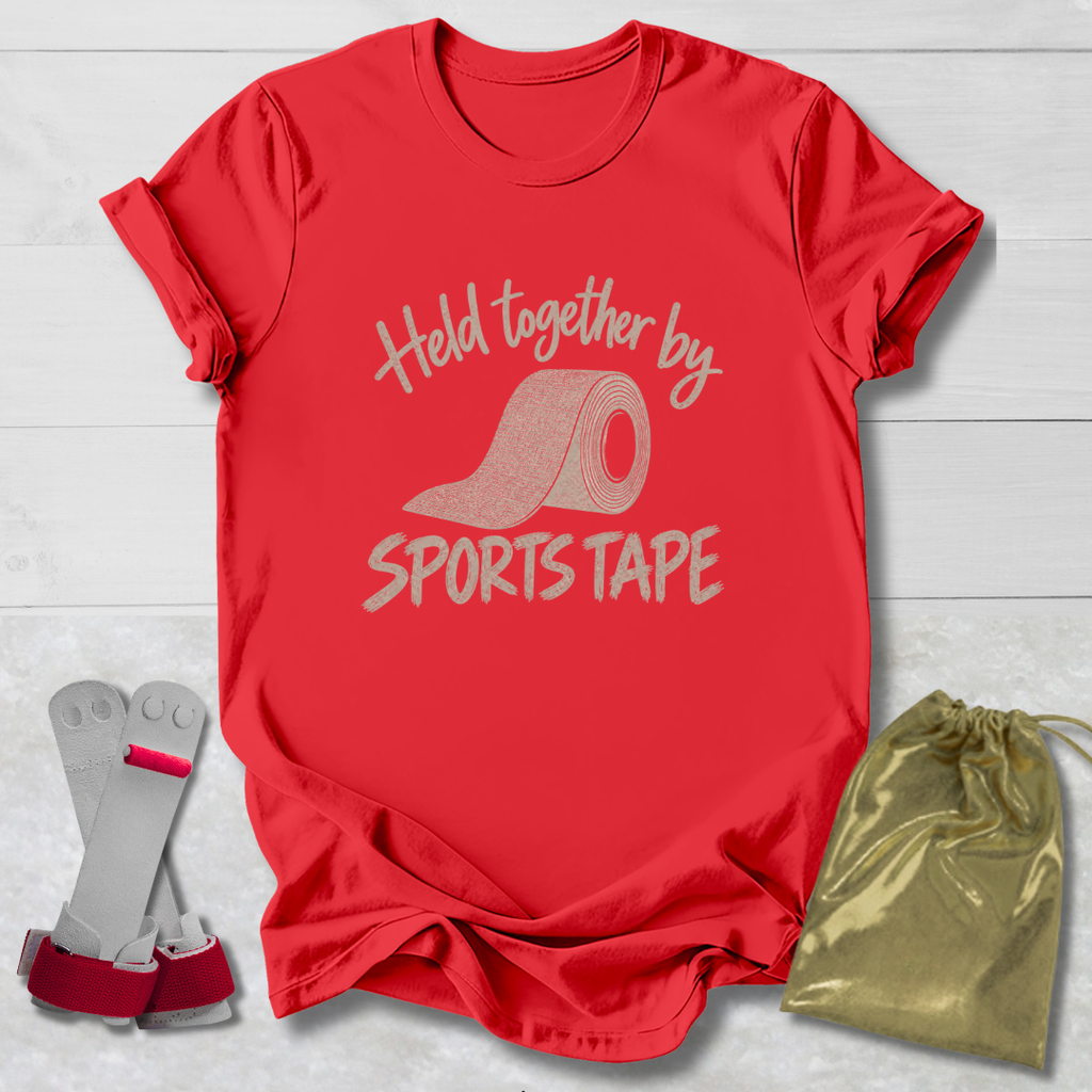 A red short-sleeve T-shirt laid flat on a white wood background, printed with the phrase 'Held together by SPORTS TAPE' and a roll of sports tape graphic. A pair of white and red athletic wrist wraps and a shiny gold drawstring pouch are placed beside the shirt as included accessories or related items.