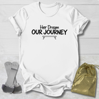 A white short-sleeve T-shirt laid flat on a light wood background, printed with the black text 'Will trade brother for a new leopard' across the chest. Two small accessories are placed beside it: a pair of gray straps on the left and a shiny gold drawstring pouch on the right.