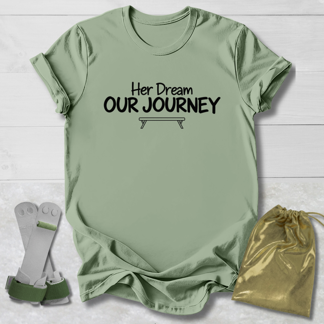 A sage green graphic t-shirt with the black printed text 'Her Dream OUR JOURNEY' and a small bench graphic, displayed on a white wood background alongside a pair of white and green support braces and a gold drawstring bag.