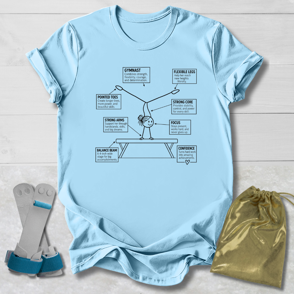 A light blue graphic t-shirt laid flat on a white wood background, featuring a gymnast diagram with labels. A gold drawstring bag and a pair of blue and gray gymnastic straps are placed beside the shirt.