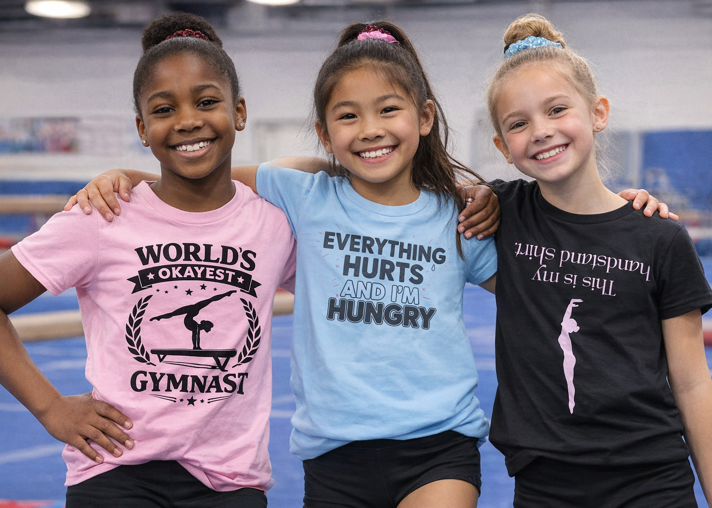 Three young girls posing together with humorous t-shirts in a gym setting